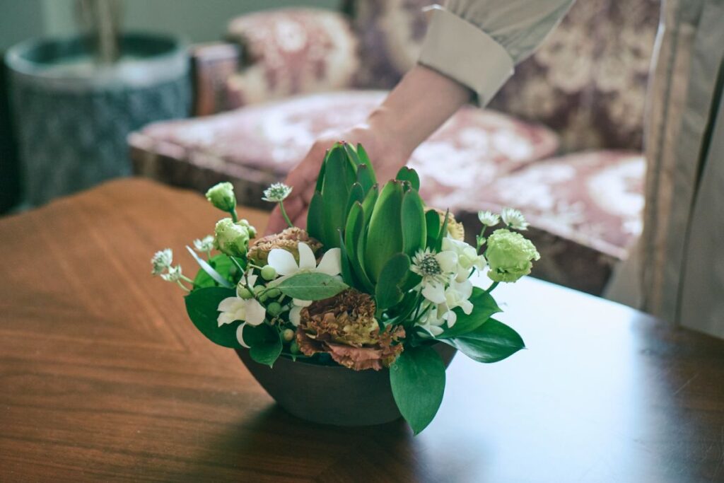 机の上に置かれた花のアレンジメントに手を添える女性
